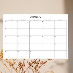 a calendar is hanging on a wall next to some dried plants and a vase with flowers in it