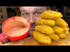 a man holding a red cup next to a stack of fried doughnuts and dipping sauce