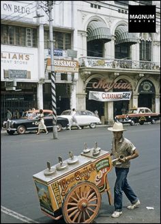 a man pushing a cart down the street with an ice cream vendor on it's back