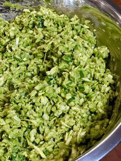 a metal bowl filled with green food on top of a wooden table