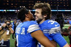 two football players hugging each other on the field at a stadium with cameras around them