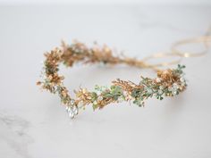 a gold headpiece with flowers and leaves on it's side, sitting on a marble surface