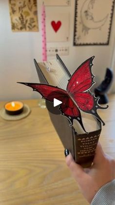 a person holding a book with a red butterfly on it's cover and the pages are open