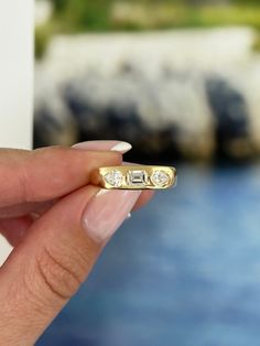 a woman's hand holding a gold ring with two diamonds on it and water in the background