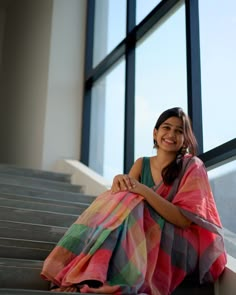 a woman sitting on the steps in front of a window with a colorful blanket over her