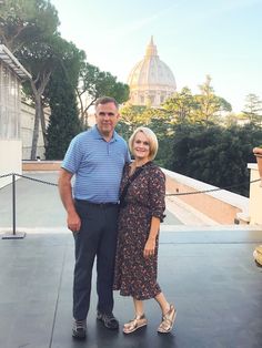 two people standing next to each other in front of a building with a dome on top