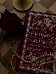 a red book sitting on top of a table next to a rose and pearls necklace