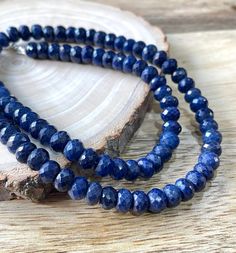 two strands of blue lapel beads sitting on top of a piece of drift wood