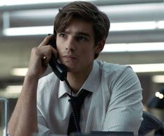 a man sitting at a desk talking on a cell phone while wearing a shirt and tie