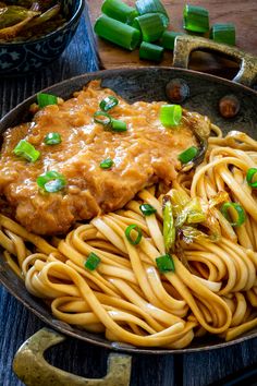 a bowl filled with pasta and sauce on top of a wooden table next to chopsticks