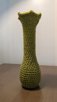 a crocheted green vase sitting on top of a wooden table next to a white wall