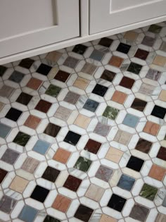 a bathroom with white cabinets and multicolored tiles on the floor