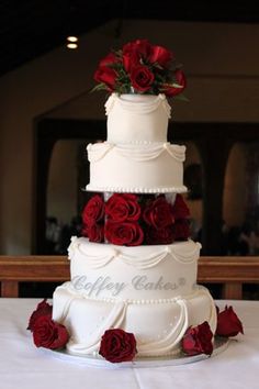 a three tiered wedding cake with red roses on the top and bottom, sitting on a table