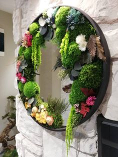 a wreath made out of moss and flowers is hanging on the wall next to a fireplace