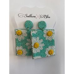 a pair of beaded earrings with yellow and white flowers on green fabric, hanging from a card