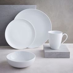 white dishes and cups sitting on top of each other next to a block of concrete