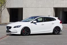 a white car parked in front of a building with red rims and black wheels