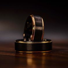 two wedding bands on top of each other in front of a black and gold watch