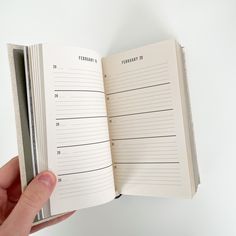 a hand holding an open planner book on top of a white surface with the pages lined up