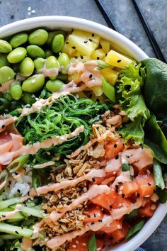 a bowl filled with different types of salads and vegetables next to chopsticks