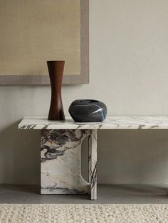 a white marble table with a black vase on it and a painting hanging above the table