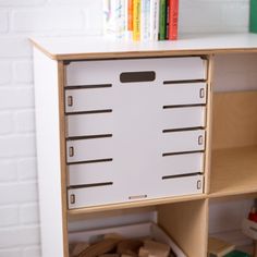 a wooden toy storage unit with lots of toys on the floor and bookshelf behind it