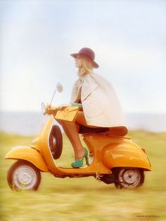 a woman riding on the back of a yellow scooter in an open field