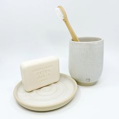 a white cup with a toothbrush in it next to a soap bar on a plate