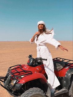 a woman standing on top of an atv in the middle of desert with her arms outstretched