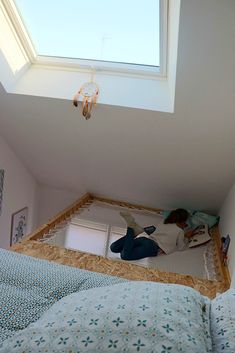 a person laying on top of a bed under a skylight in a room with white walls