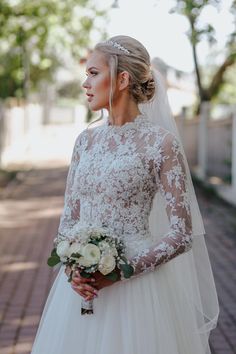 a woman in a wedding dress standing on a brick walkway holding a bouquet and looking off into the distance