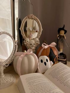 an open book sitting on top of a table next to a mirror and pumpkins