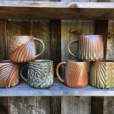 five different colored mugs sitting on top of a wooden shelf next to each other