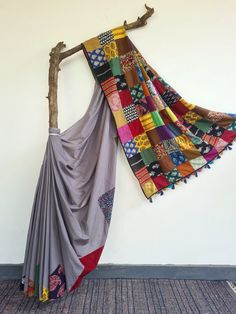 a multicolored blanket hanging on a wall next to a tree branch and rug