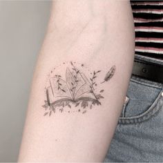 an open book tattoo on the arm with leaves and arrows coming out of it's pages