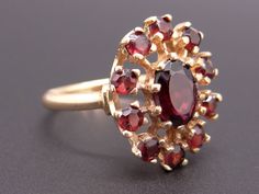 Jewelry Type: Gemstone Cluster Ring Metal: 14k Yellow Gold Measurements: 17mm by 14mm ( front face of ring) 2mm wide back of shank (most narrow area of band) 7mm high ( finger to top of ring) Weight: 3.4grams Center Stone: Oval Cut Garnet Center Stone Measurements: 7mm * 5mm * 2.8mm Gem Weight: 0.50ct approx Accent Stones: 10 matching Round Brilliant Cut Garnet Gem Weight: 0.80ct total approx US Finger Size: 6 #8758 Rosé Angel, Garnet Gem, Front Face, Adjustable Jewelry, Wide Band Rings, Ring Metal, Pretty Rings, Ruby Diamond, Anniversary Bands