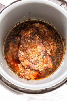 an open crock pot filled with meat and vegetables on top of a white table