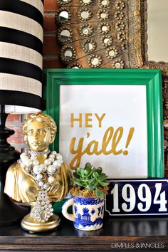 a gold and green framed sign sitting on top of a table next to a cup