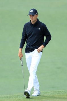 a man in black shirt and white pants holding a golf club while standing on a green field