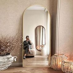 a man sitting on a stool in front of a large mirror next to a potted plant