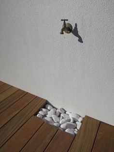 a white wall with a faucet and some rocks on the ground next to it