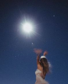 a woman in white dress flying through the air under a full moon and stars filled sky