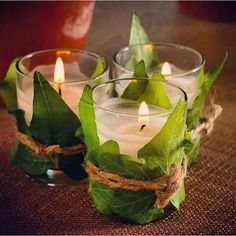 three glass candles with green leaves and twine around them on a brown table cloth