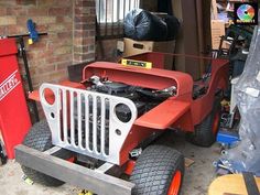 an old red jeep is parked next to a brick wall in a garage with other tools on the ground