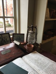 an open book sitting on top of a wooden table next to a lamp and window