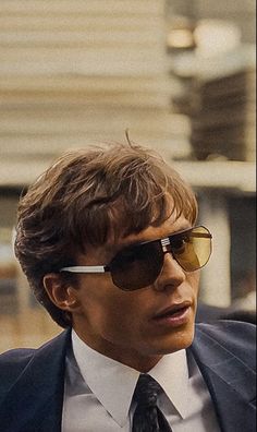 a man in a suit and tie with sunglasses on looking off to the side,