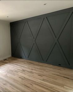 an empty room with hard wood floors and gray wall paneling on the walls, in front of a window