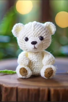 a crocheted white teddy bear sitting on top of a wooden table with lights in the background