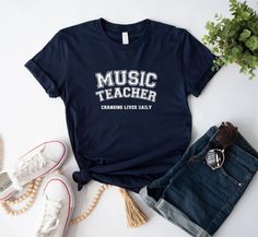 🌟 Welcome to Comzy Closet! 🌟 Do you like this "Music Teacher: Changing Lives Daily" t-shirt?  We are working hard, to get the best tees in town for YOU! Support our small business and buy our cozy t-shirts! You won't regret!  Step into a world of your unique style add a touch of individuality to your wardrobe with our collection of custom design printed tees!  🎨 Express Yourself: From vibrant graphics to intricate patterns, our designs are crafted to ignite your imagination and make a stateme Cotton Music-themed T-shirt With Text Print, Band Merch Cotton Tops For School, Cotton Band Merch Tops For School, School Cotton Tops With Band Merch Style, School Tops In Cotton With Band Merch Style, Unisex Music-themed Cotton T-shirt, Elementary Music Teacher, Music Teacher Gifts, School Tops