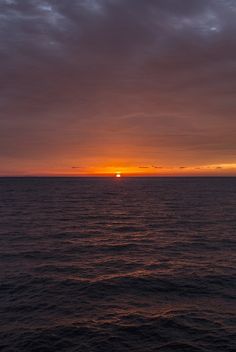 the sun is setting over the ocean as seen from a boat on the water with dark clouds